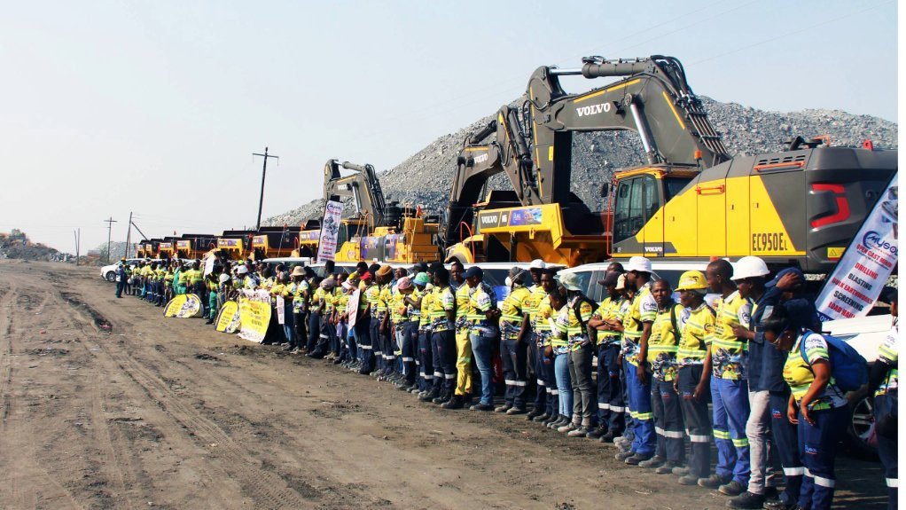 MySol employees in high-visibility clothing lined up in front of Volvo excavators